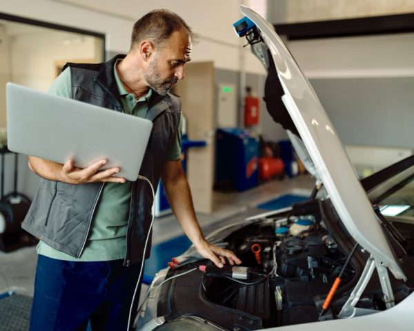 auto-repairman-using-laptop-while-examining-car-engine-workshop